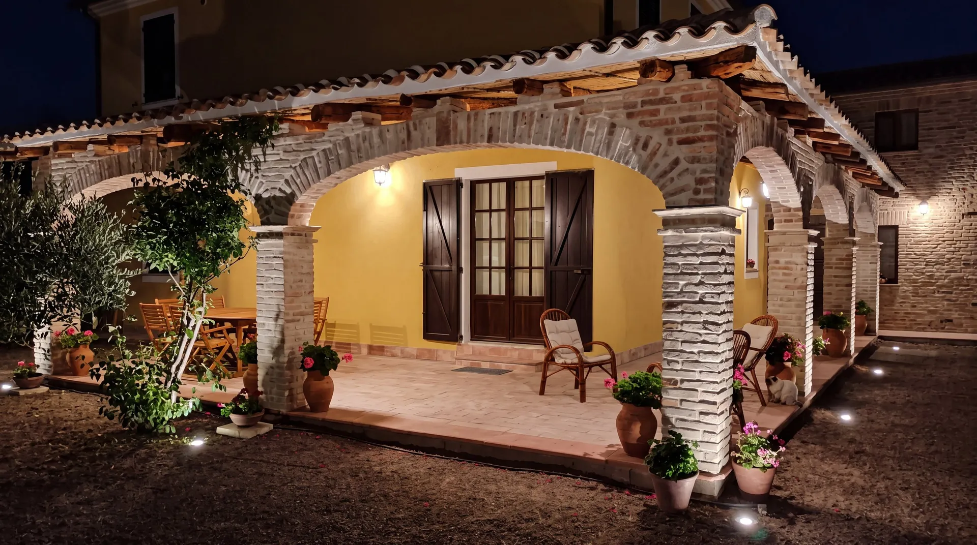 Campidano-style veranda with reclaimed brick arches, lit at dusk, in Santa Margherita di Pula